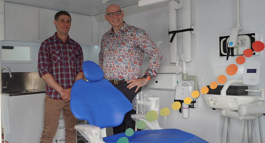 Two men standing inside a dental van.