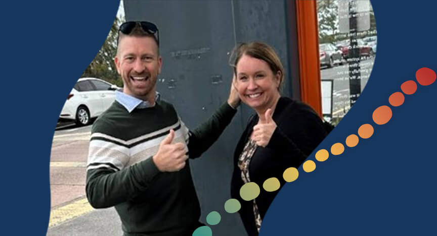 Two people standing outside in front of a pole, smiling.